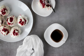 Homemade dessert Pavlova with raspberries on a white plate and two white cups of coffee on a gray table.