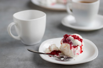 Homemade dessert Pavlova with raspberries on a white plate and two white cups of coffee on a gray table.