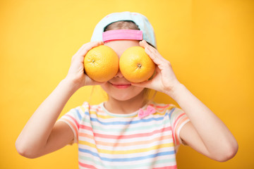 Smiling child girl holding two yellow grapefruit citrus fruit in hands, covering her eyes. Healthy...