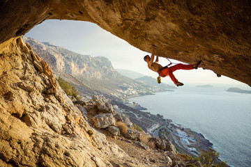 Young man climbing challenging route in cave against beautiful view of coast