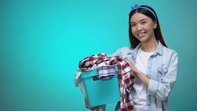 Cheerful woman holding laundry basket and smiling at camera, template for text