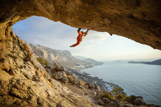 Young man climbing challenging route in cave against view of coast