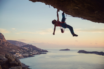 Young man struggling to climb challenging route on cliff