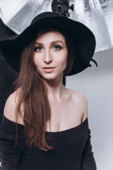 Close up portrait of young caucasain brunette sexy professional model posing in photo studio in black hat making photosession for advertising. Modeling, posing, fashion beauty concept