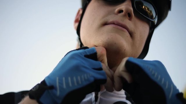 A man buckling up his bicycle helmet. The man is looking straight ahead and has a serious expression on his face.