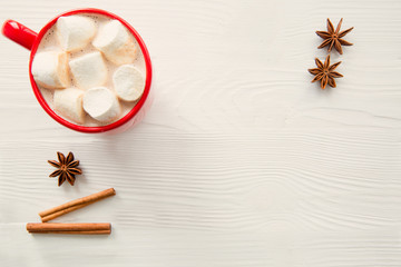 A red cup of hot cocoa with marshmallow on white wooden table, space for text, copy space. Christmas background. 