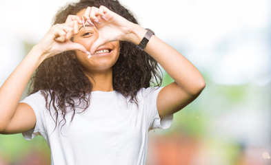 Young beautiful girl with curly hair wearing casual white t-shirt Doing heart shape with hand and fingers smiling looking through sign