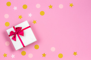Festive gift box with satin bow and glitter confetti sparkles on light pastel pink background. Top view