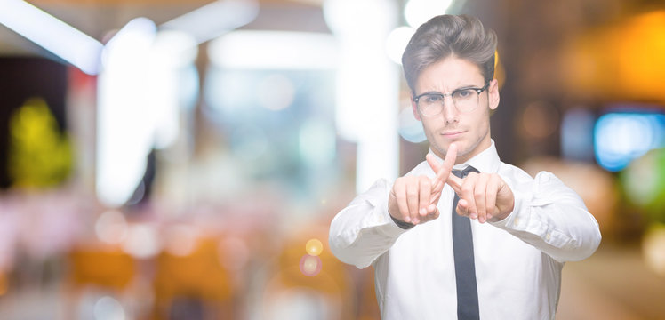 Young business man wearing glasses over isolated background Rejection expression crossing fingers doing negative sign