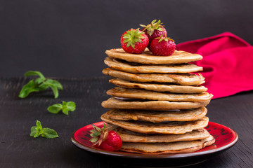 Delicious pancake with strawberries on black table.