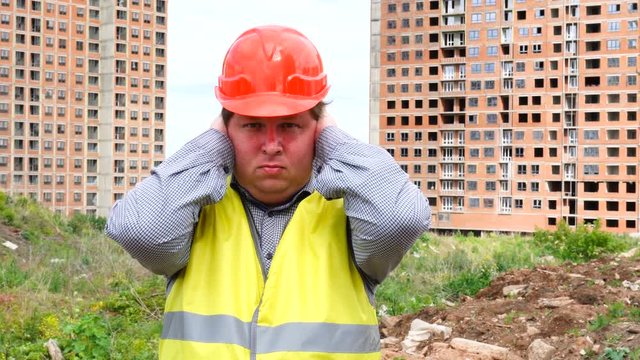 young handsome builder is afraid (man covers his ears with hands) - construction site