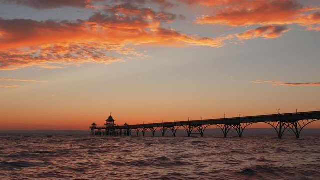 Beautiful vibrant sunset over ocean, with silhouette of pier