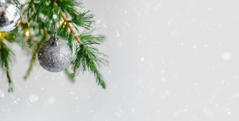 New Year's silver shiny ball hanging on a fir branch. Lights and garlands on a gray snow background. Christmas and happy new year concept, space for text for your design. Wallpaper.