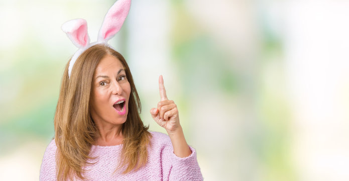 Middle age brunette woman wearing easter rabbit ears over isolated background pointing finger up with successful idea. Exited and happy. Number one.