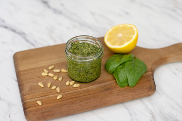 Homemade Pesto in a Small Jar Surrounded by Pine Nuts, Basil, and Lemon
