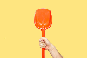 Concept of summer, childhood, be a child, playing in the beach, be in a holiday, end of the shool. Hand holding an orange beach shovel. Yellow background
