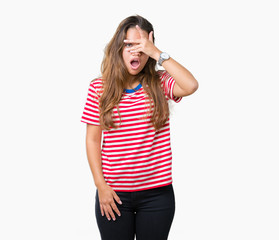 Obraz na płótnie Canvas Young beautiful brunette woman wearing stripes t-shirt over isolated background peeking in shock covering face and eyes with hand, looking through fingers with embarrassed expression.