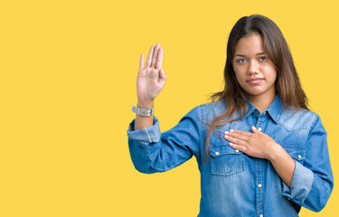 Young beautiful brunette woman wearing blue denim shirt over isolated background Swearing with hand...