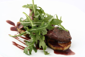 Meat medallions with roasted zucchini with fresh arugula. With red sauce. Close-up on a white plate