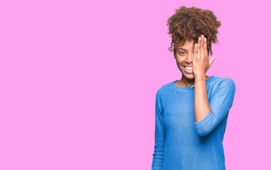 Fototapeta na wymiar Beautiful young african american woman over isolated background covering one eye with hand with confident smile on face and surprise emotion.