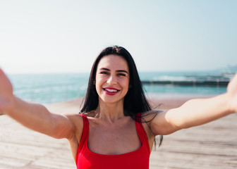 Portrait of young smiling woman in a red swimsuit takes a selfie on the beach