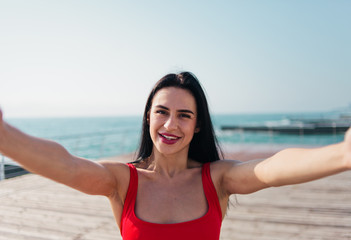 Portrait of young smiling woman in a red swimsuit takes a selfie on the beach