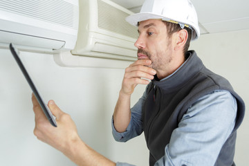 happy male technician repairing air conditioner with screwdriver