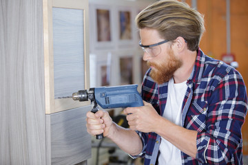 man drilling a nail into a wood wall