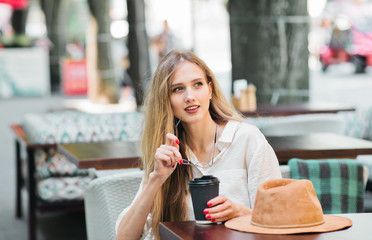 Cheerful smiling blond woman sits in a street cafe and drinks coffee
