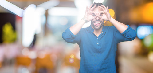 Young handsome man over isolated background doing ok gesture like binoculars sticking tongue out, eyes looking through fingers. Crazy expression.