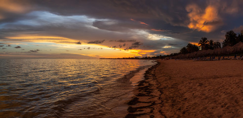 Beautiful Panoramic view of a sandy beach, Playa Ancon, on the Caribbean Sea in Triniday, Cuba, during a dramatic cloudy sunset.