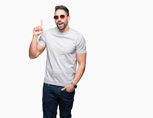 Fototapeta premium Young handsome man wearing sunglasses over isolated background pointing finger up with successful idea. Exited and happy. Number one.