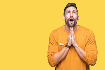 Obraz premium Young handsome man over isolated background begging and praying with hands together with hope expression on face very emotional and worried. Asking for forgiveness. Religion concept.