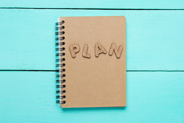 I have an plan! Notebook with craft paper with word PLAN on blue wooden table.