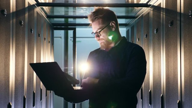 Data center worker checks server computers, typing on a laptop. Computer system security specialist.