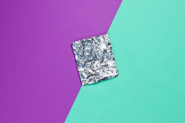 A piece of foil on colored paper background. Top view. Minimalism concept