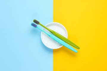 Two toothbrushes, tooth powder on yellow blue background. Minimalism oral hygiene concept. Top view