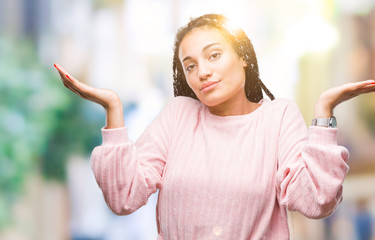 Young braided hair african american girl wearing sweater over isolated background clueless and...