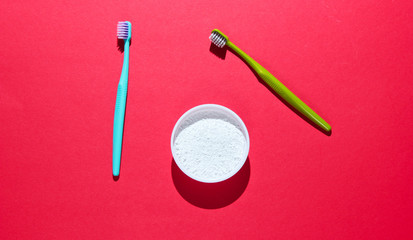 Two toothbrushes, tooth powder on red background. Minimalism oral hygiene concept. Top view