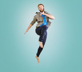 Full-length photo of beard man in casual t-shirt and jeans running or jumping in air makes funny faces over blue background