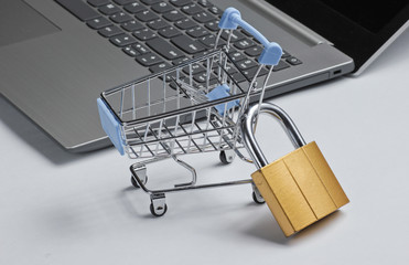 Restriction on online shopping minimalistic concept. Mini shopping trolley with lock, laptop on...