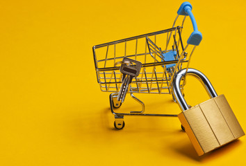 Minimalistic shopping concept. Mini shopping trolley with a lock on yellow background.