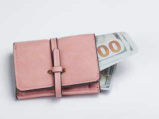 Leather pink purse with hundred dollar bills on a white background
