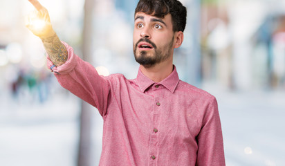 Young handsome man wearing pink shirt over isolated background Pointing with finger surprised ahead, open mouth amazed expression, something in front