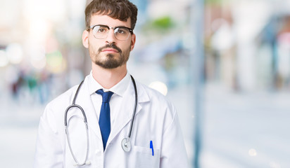 Young doctor man wearing hospital coat over isolated background Relaxed with serious expression on face. Simple and natural looking at the camera.