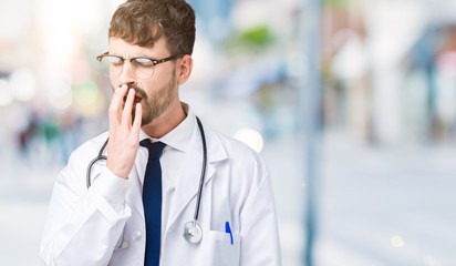 Young doctor man wearing hospital coat over isolated background bored yawning tired covering mouth...