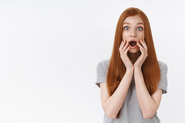 Shocked amused speechless ginger girl popping blue eyes drop jaw impressed touch face standing...