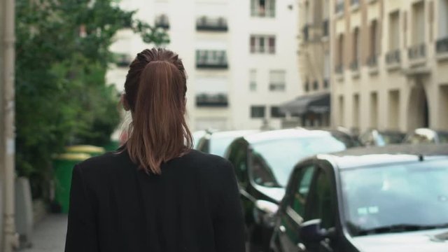 Follow-up Shot of classy confident caucasian woman with sunglasses, freckles, piercings, ponytail, jacket and red hair walking through the street, during sunny day in Paris. Slow motion Back View.