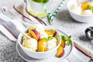  Homemade peach ice cream with mint and fresh peach slices in a plate on a gray background