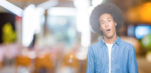 Young african american man with afro hair In shock face, looking skeptical and sarcastic, surprised...